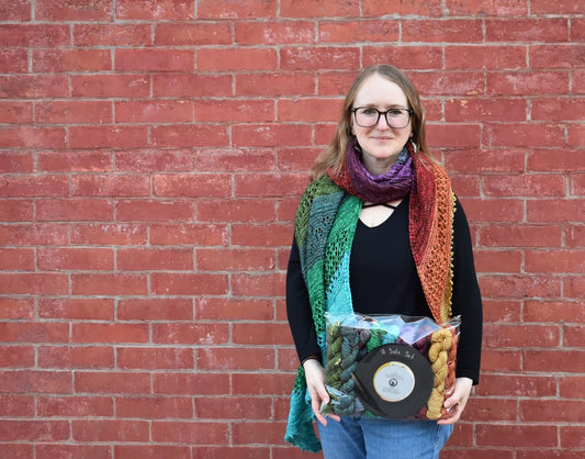 Person holding a vinyl record and colorful package against a red brick wall