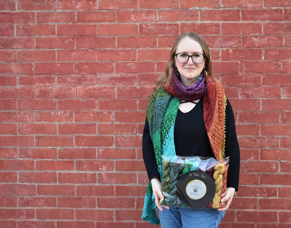 Person holding a vinyl record and colorful package against a red brick wall