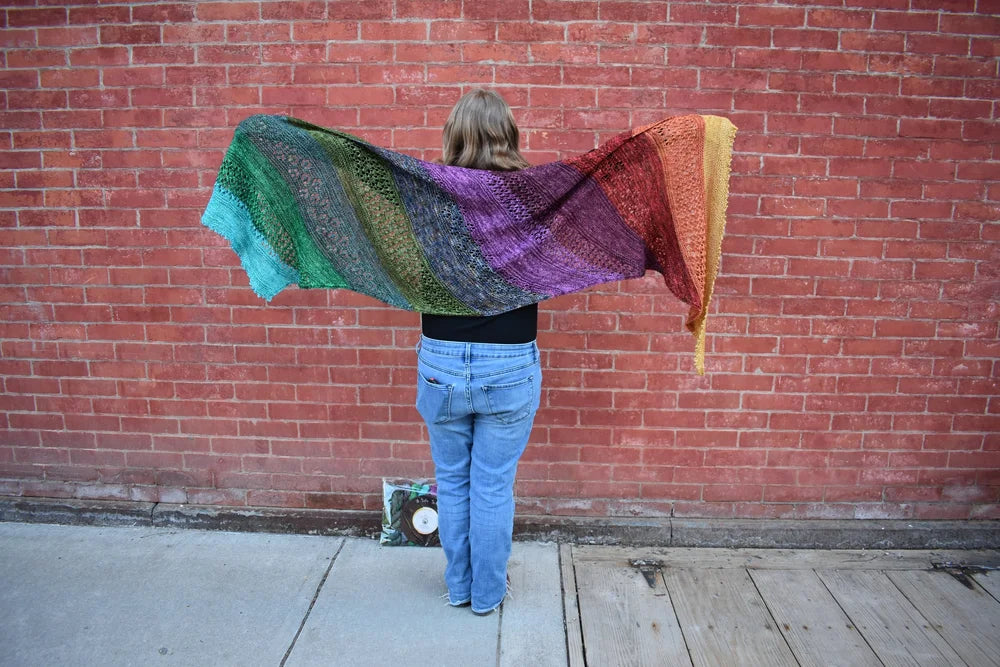 Person holding a colorful shawl in front of a brick wall