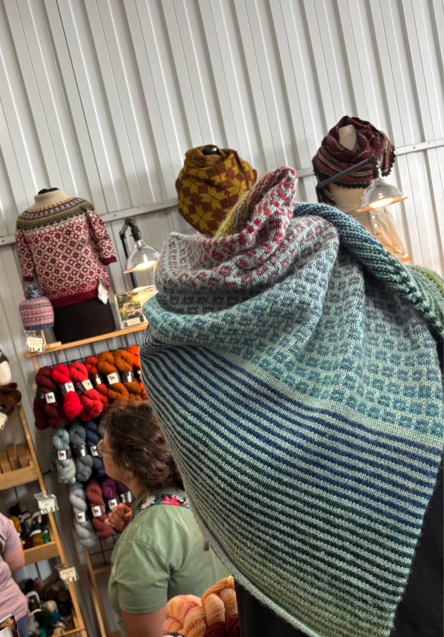 Knitted items on display in a yarn store with people browsing.