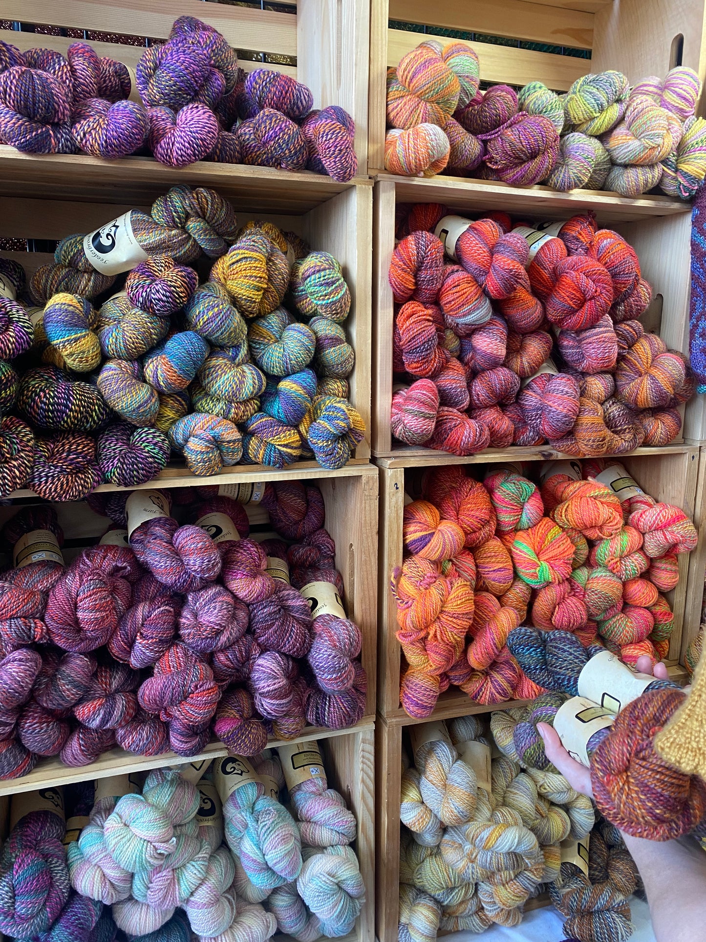 Colorful yarn skeins in wooden crates with a person wearing a knitted hat.
